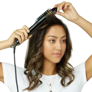 A person is using a heated styling brush on their hair. The brush has a cord and is designed for straightening or styling.