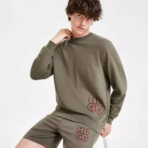 A man is wearing a matching olive green sweatshirt and shorts set with the HUGO logo.