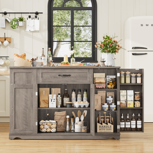 A kitchen island features an assortment of pantry items including oils, spices, pasta, tea, coffee, cereals, and baking supplies, with a countertop holding bread, drinks, and a floral arrangement, surrounded by a sleek, modern kitchen setup.