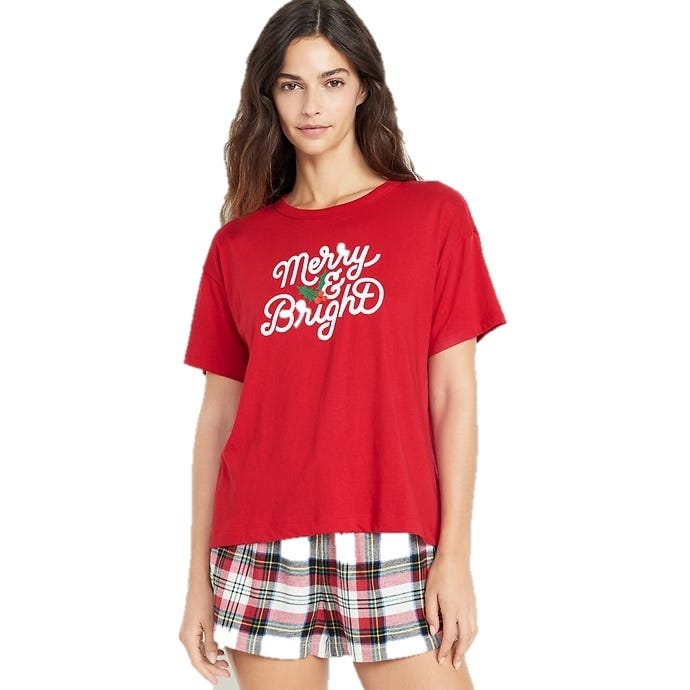 Red T-shirt with \“Merry & Bright\“ in white script and a small green holly design, paired with plaid shorts.