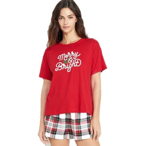 Red T-shirt with \“Merry & Bright\“ in white script and a small green holly design, paired with plaid shorts.