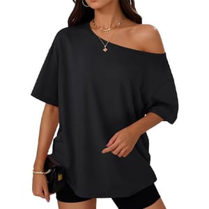 A woman is wearing a loose-fitting black off-shoulder top, paired with black shorts and accessorized with gold necklaces and a bracelet, holding a black clutch.