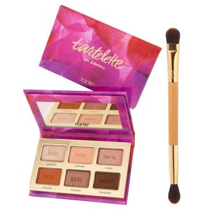 Tartelette in Bloom palette features six eyeshadow shades, including Go-Getter, Innovator, and Trendsetter, in a vibrant purple and pink case. Accompanied by a dual-ended brush for application.