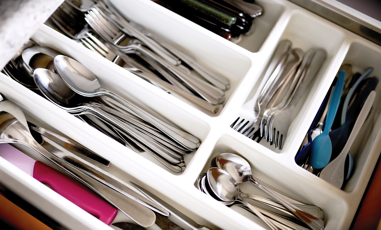 Assorted cutlery organized in a drawer divider, including forks, spoons, and knives.
