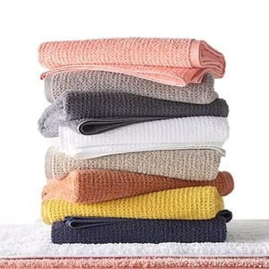 A stack of towels in various colors, including pink, gray, white, beige, orange, yellow, and navy, with a textured, waffle-like pattern.
