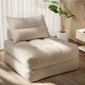 A beige, plush floor chair with a matching pillow is set in a room with a potted plant and a side table.