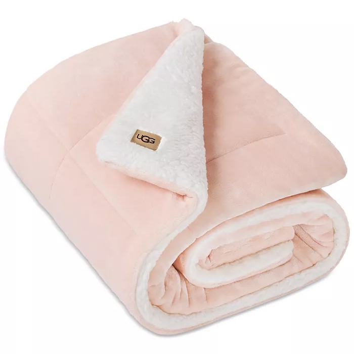 A folded pink blanket with a soft, white sherpa lining and a small tag labeled \“UGG\“ on one corner.