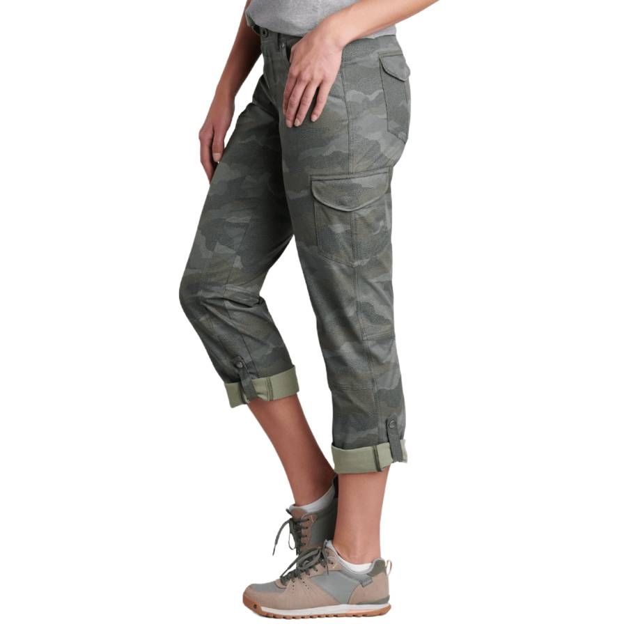 Kuhl Roll-Up Pants feature a camo pattern with a roll-up design secured by button tabs, side cargo pockets, and are paired with gray hiking shoes.