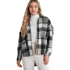 A woman wearing a black and white plaid button-up jacket over a white turtleneck sweater, paired with light-colored pants.