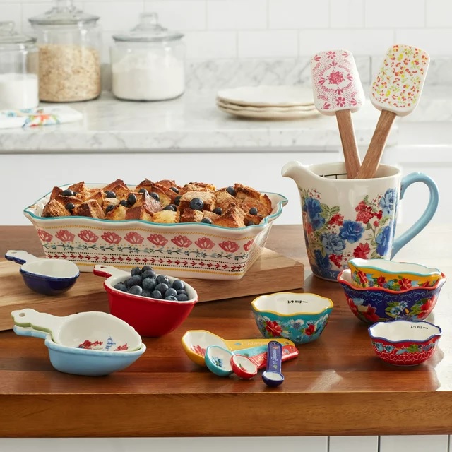 Colorful patterned bakeware and utensils including measuring cups, spoons, a jug, and a baking dish with bread pudding.