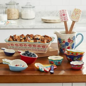 Colorful patterned bakeware and utensils including measuring cups, spoons, a jug, and a baking dish with bread pudding.