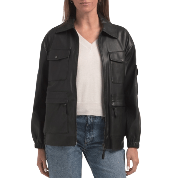 A black faux leather jacket with a zip front, featuring multiple pockets, elastic cuffs, and a collar, worn over a white V-neck top and blue jeans.
