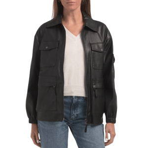 A black faux leather jacket with a zip front, featuring multiple pockets, elastic cuffs, and a collar, worn over a white V-neck top and blue jeans.