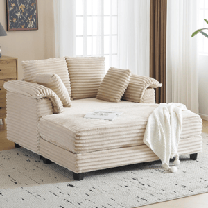 A beige corduroy chaise lounge with ribbed cushions, placed on a patterned rug. A throw blanket is draped over the seat, and it's set in a light-filled room with a wooden dresser and decorative items.