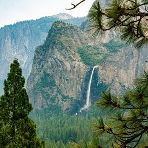Lush greenery surrounds a tall waterfall cascading down a cliff face.