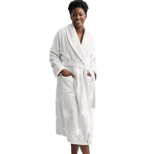 A woman wears a white bathrobe with a subtle polka dot pattern, featuring a shawl collar, waist tie, and two front pockets.