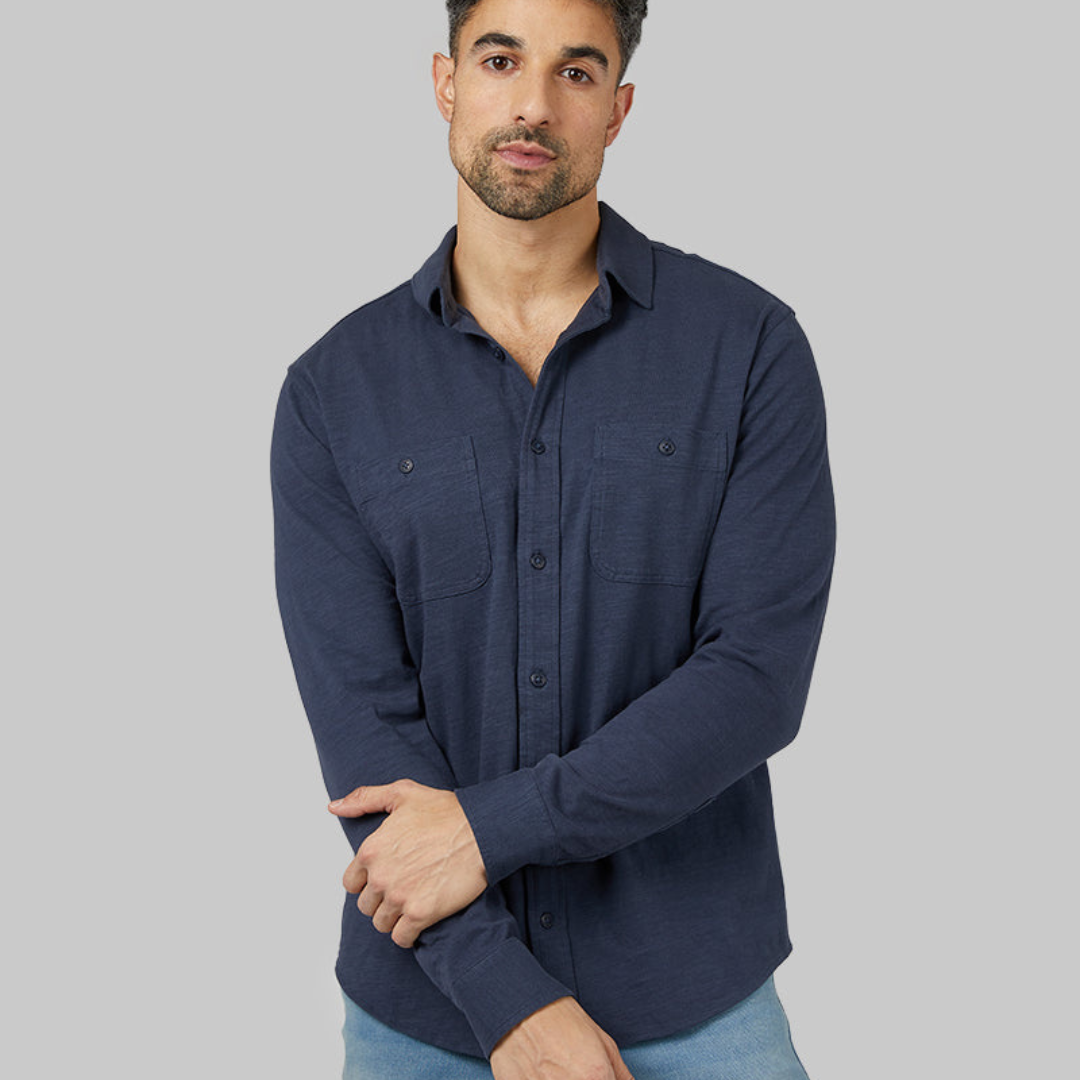 A man wearing a navy blue button-up shirt with two chest pockets and light blue jeans.