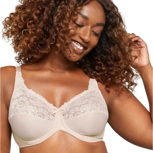A woman is wearing a beige lace bra with intricate floral details and underwire support, smiling and touching her curly hair.