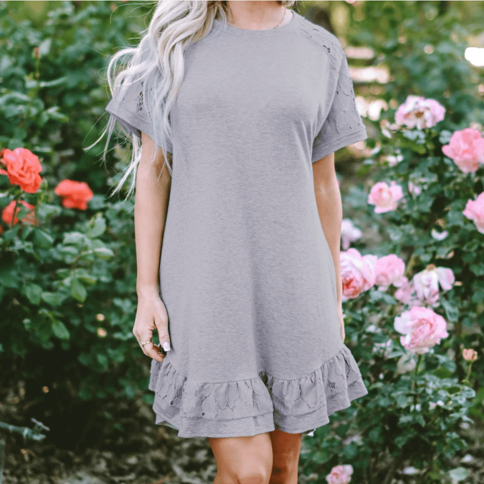 A gray dress with short lace sleeves and a ruffled hem against a backdrop of rose bushes.