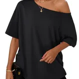 A woman is wearing an off-the-shoulder short-sleeve black top paired with black shorts. She accessorizes with gold necklaces, hoop earrings, and a bracelet, and is holding a small black clutch.