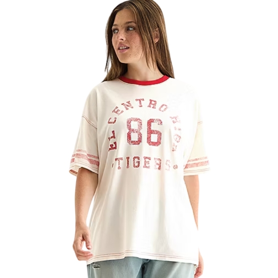 A woman wears a white vintage-style T-shirt with red accents, featuring \“El Centro High Tigers\“ and \“86\“ printed on the front, paired with light blue jeans.
