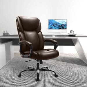 A brown leather executive chair with a high backrest and padded armrests sits in front of a modern desk with a computer monitor.