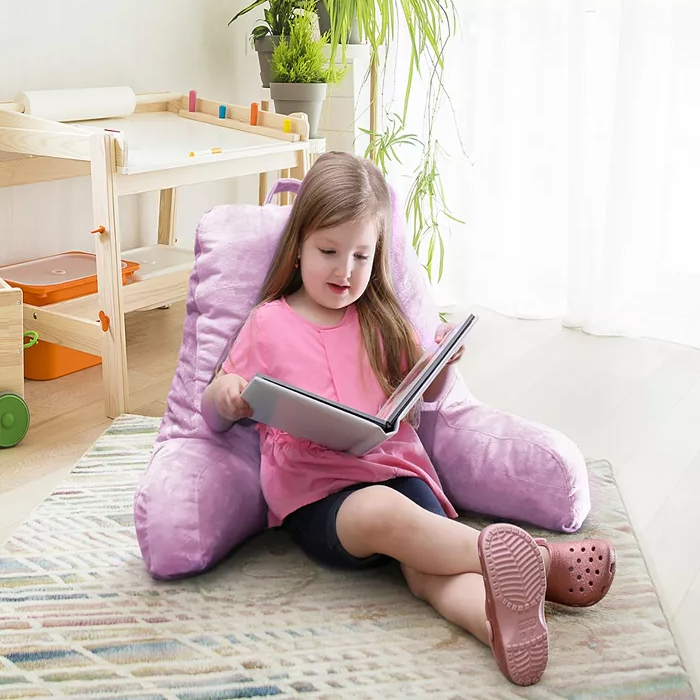 A young girl sits in a large, plush purple chair with a book in her hands.