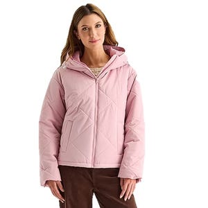 A woman is wearing a light pink padded jacket with a hood and front zipper, paired with brown pants.