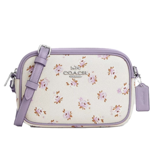 A Coach camera bag with a cream base featuring a purple floral pattern, accented by lavender trim and an adjustable lavender strap.