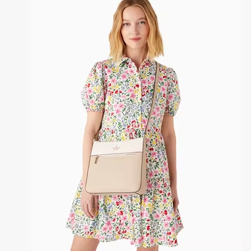 A woman is wearing a floral dress and carrying a beige crossbody bag.
