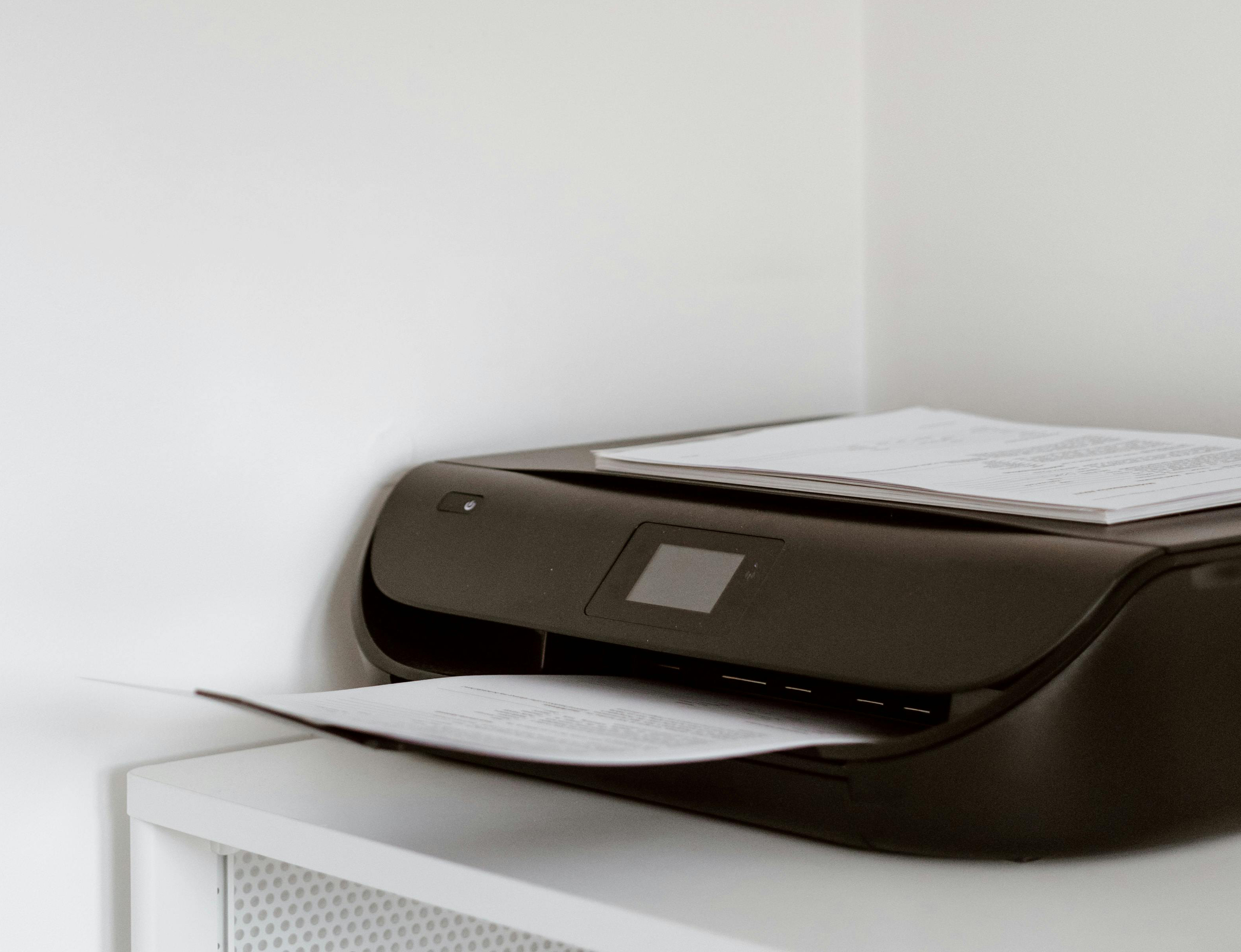 A black printer with papers on top, placed on a white cabinet.