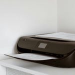 A black printer with papers on top, placed on a white cabinet.