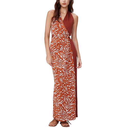 The Diane Von Furstenberg Chase Dress features a halter neck design with a striking asymmetric pattern in rust and white, blending solid and printed panels for an elegant look. It is a floor-length dress worn with sandals.