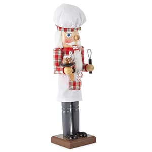 A nutcracker figurine dressed as a baker, featuring a chef hat, red plaid shirt, white apron, brown pants, and holding a rolling pin and a cake.