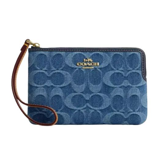 A Coach wristlet with a blue denim finish featuring the brand's signature \“C\“ monogram pattern and a brown leather strap.