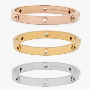 Three bangle bracelets in rose gold, gold, and silver colors displayed with a designer logo engraved.