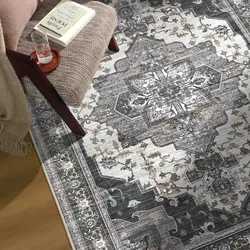 A patterned area rug with intricate designs in neutral tones is shown beneath a chair, which holds a book and a glass of water on a small tray.