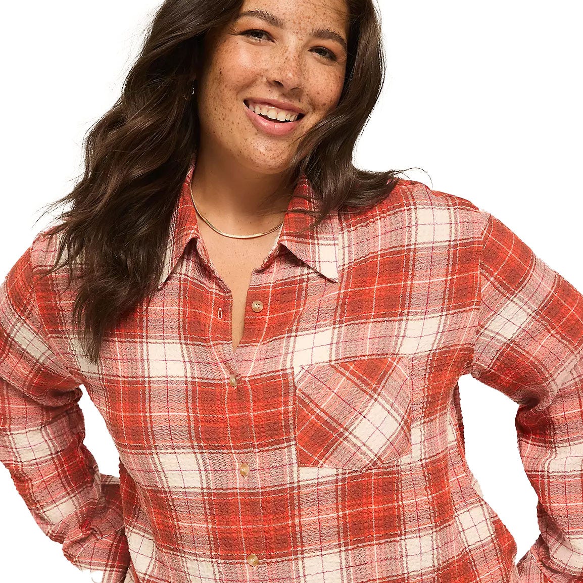 A woman is wearing a red and white plaid flannel shirt with a single chest pocket and button-down collar. She has long, wavy dark hair and is smiling.