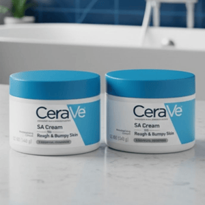 Two jars of CeraVe SA Cream for Rough & Bumpy Skin, each containing 12 oz (340 g), are displayed on a bathroom countertop with a blue-tiled wall and a bathtub in the background.