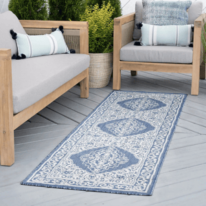 Outdoor seating area featuring wooden furniture with gray cushions, blue and white decorative pillows, and a blue patterned runner rug.