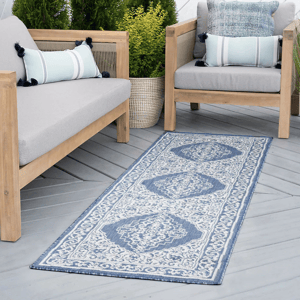 Outdoor seating area featuring wooden furniture with gray cushions, blue and white decorative pillows, and a blue patterned runner rug.