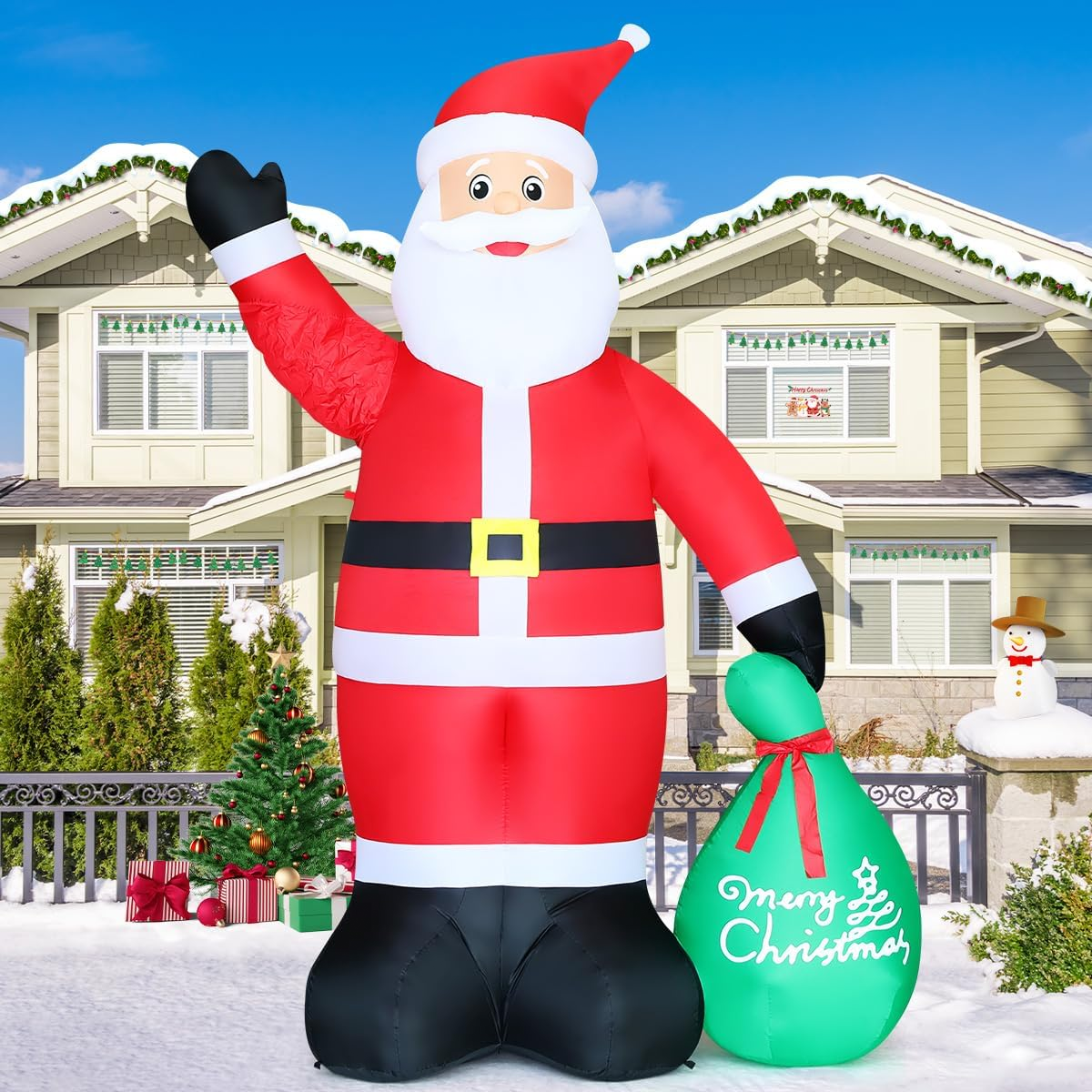 A large inflatable Santa Claus decoration is displayed in front of a house, holding a green sack with \“Merry Christmas\“ written on it.