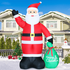 A large inflatable Santa Claus decoration is displayed in front of a house, holding a green sack with \“Merry Christmas\“ written on it.