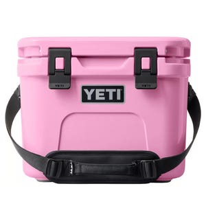 Pink YETI cooler with black latches, brand logo on the front, and a black shoulder strap.