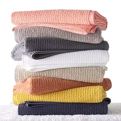 A stack of colorful waffle-knit bath towels in shades of pink, gray, white, beige, orange, yellow, and dark blue.