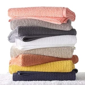 A stack of colorful waffle-knit bath towels in shades of pink, gray, white, beige, orange, yellow, and dark blue.
