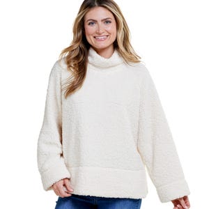The Architect Mock Neck Polar Sweatshirt is a cozy, plush, cream-colored top with a loose fit and long sleeves, featuring a high collar.