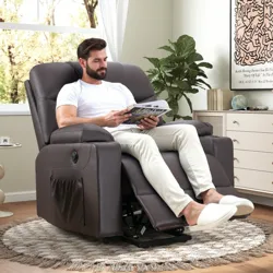 A man sits in a reclining chair with an attached side pocket, reading a magazine. The room features light décor, a round rug, a small side table with a plant, and a dresser with a Keith Haring artwork on the wall.