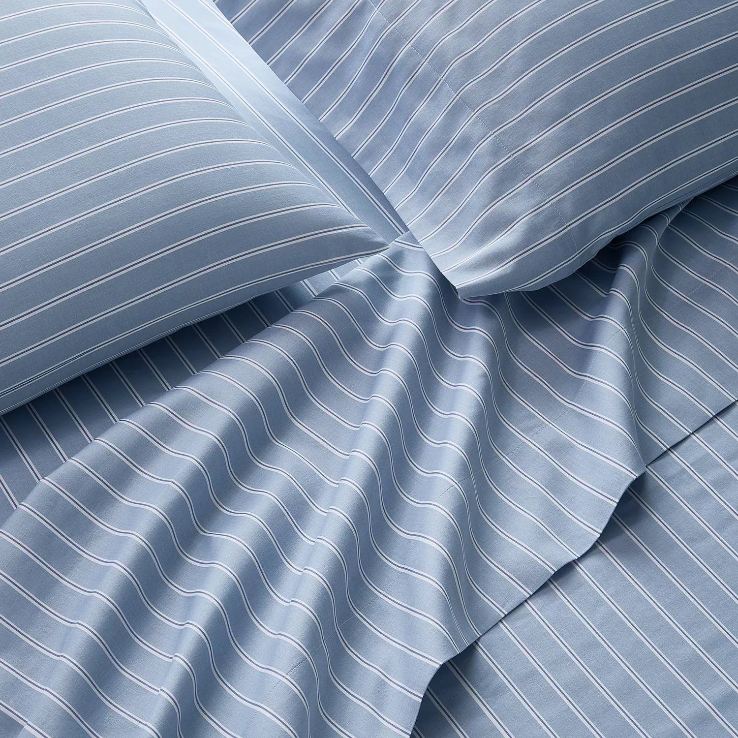 Blue bedsheets with white pinstripes, including pillowcases and a flat sheet, arranged to show texture and design.