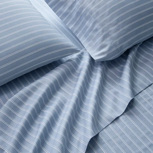 Blue bedsheets with white pinstripes, including pillowcases and a flat sheet, arranged to show texture and design.